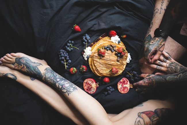 Una pareja con un pastel de cerezas y fresas encima una cama