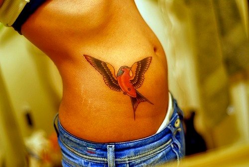 Diseño de pájaro anaranjado de alas abiertas, situado en el torso de esta chica
