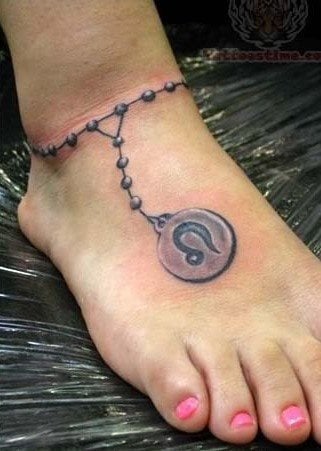Tatuaje en el pie de una cadena que bien podría parecere un rosario y cuyo remate final es una pequeña medalla con el signo zodiacal Leo tatuado en su interior
