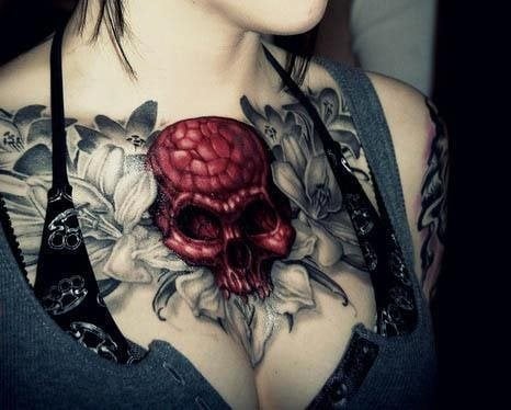Calavera muy roja que resalta sobre este tatuaje con fondo de flores de sombras, todo tatuado en el pecho de esta chica