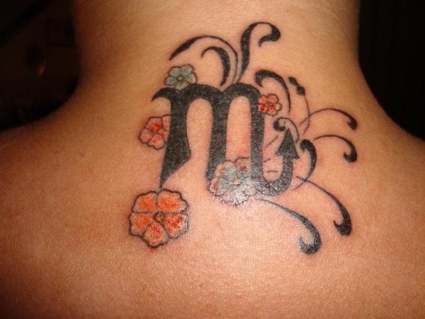 Tatuaje del signo zodiacal Escorpio a color negro sobre la nuca de una chica y para el que se ha decorado con unas pequeñas flores naranjas y otras turquesas, completado con unos pequeños ramilletes en color negro que dan un toque muy sensual a este tatuaje
