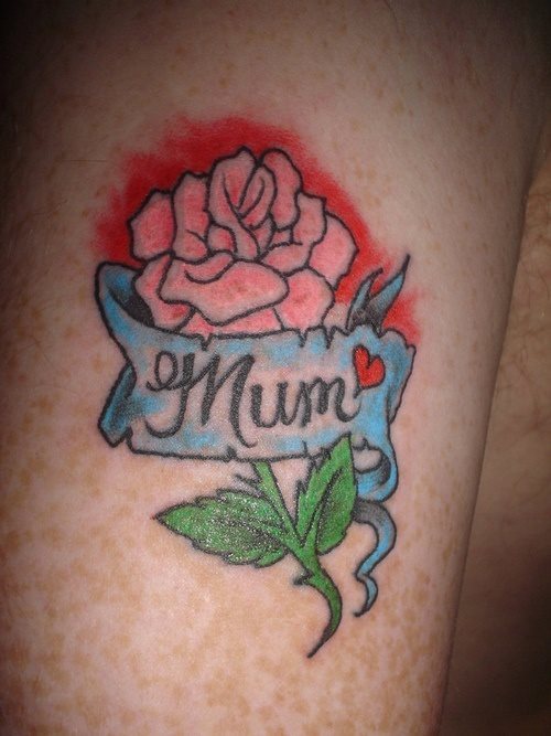 Tatuaje de una flor rosa con el fondo rojo y en el que se aprecia un lazo agrietado con la palabra mum y que se ha finalizado la palabra con un pequeño corazón de color rojo, para así dejar más claro si cabe, el gran amor que se siente hacia una madre, que todas son unas rosas