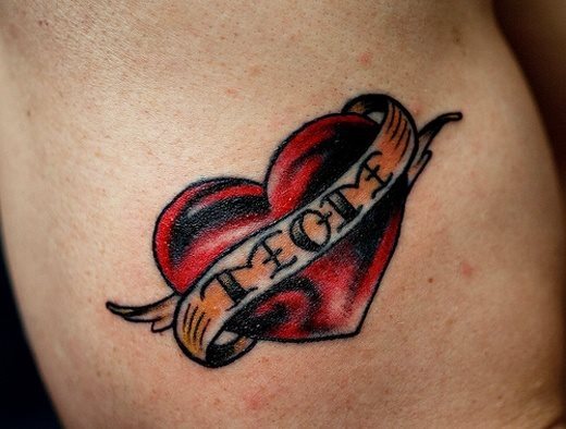 Pequeño y delicado tatuaje de un corazón rojo envuelto por un lazo blanco y amarillo con la palabra mom que termina el lazo con unos pequeños dibujos que parecen darle una imagen de alas al corazón